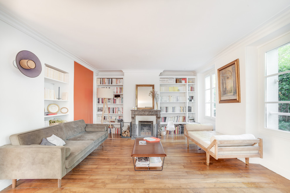 Inspiration for a transitional open concept living room in Paris with a library, orange walls, light hardwood floors, a standard fireplace, no tv and beige floor.