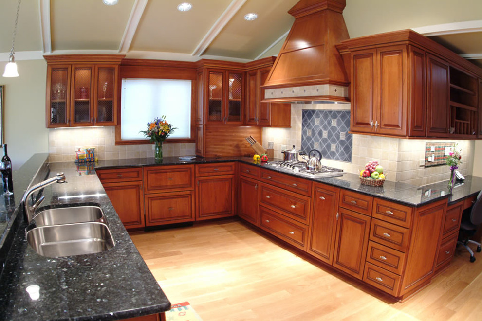 Inspiration for a large traditional u-shaped eat-in kitchen in Chicago with beaded inset cabinets, medium wood cabinets, granite benchtops, beige splashback, porcelain splashback, stainless steel appliances, a peninsula, black benchtop, a double-bowl sink, light hardwood floors and beige floor.