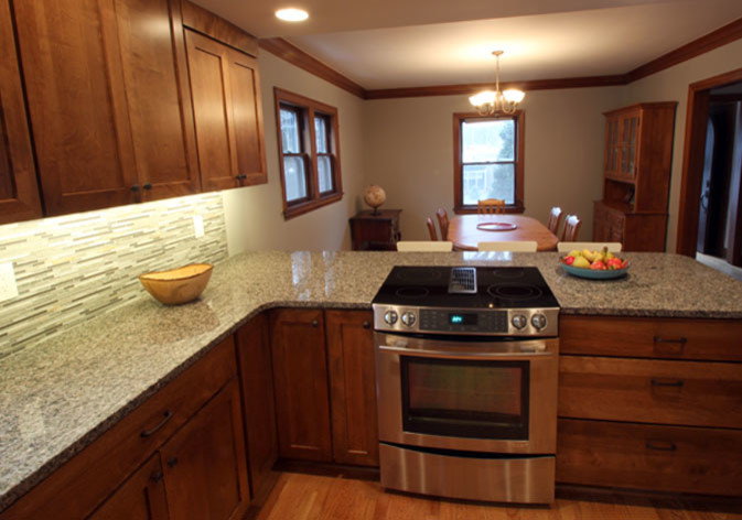 Example of a mid-sized transitional l-shaped light wood floor eat-in kitchen design with an undermount sink, shaker cabinets, dark wood cabinets, granite countertops, multicolored backsplash, mosaic tile backsplash, stainless steel appliances and a peninsula