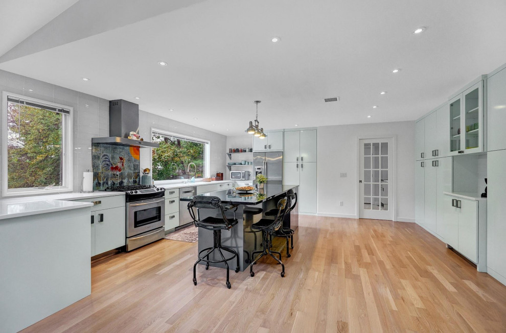 Large contemporary u-shaped eat-in kitchen in New York with an integrated sink, flat-panel cabinets, grey cabinets, granite benchtops, white splashback, glass tile splashback, stainless steel appliances, light hardwood floors, with island, beige floor and black benchtop.