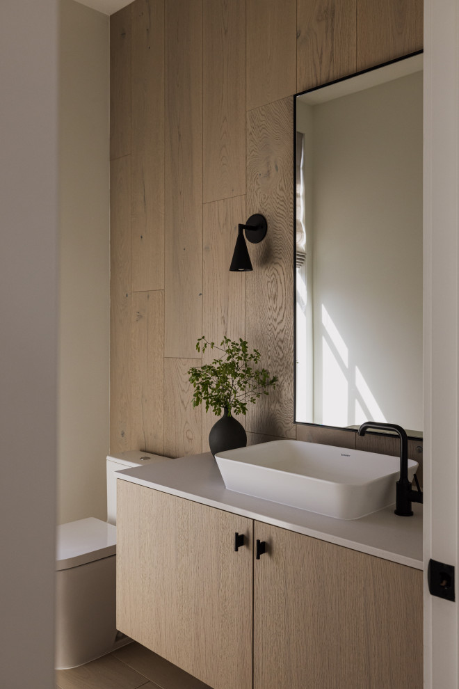 Minimalistisk inredning av ett vit vitt toalett, med släta luckor, skåp i ljust trä, beige väggar, ljust trägolv, ett fristående handfat och beiget golv