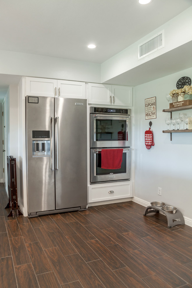Example of a mid-sized transitional u-shaped laminate floor and brown floor open concept kitchen design in Phoenix with an undermount sink, recessed-panel cabinets, white cabinets, granite countertops, multicolored backsplash, mosaic tile backsplash and stainless steel appliances