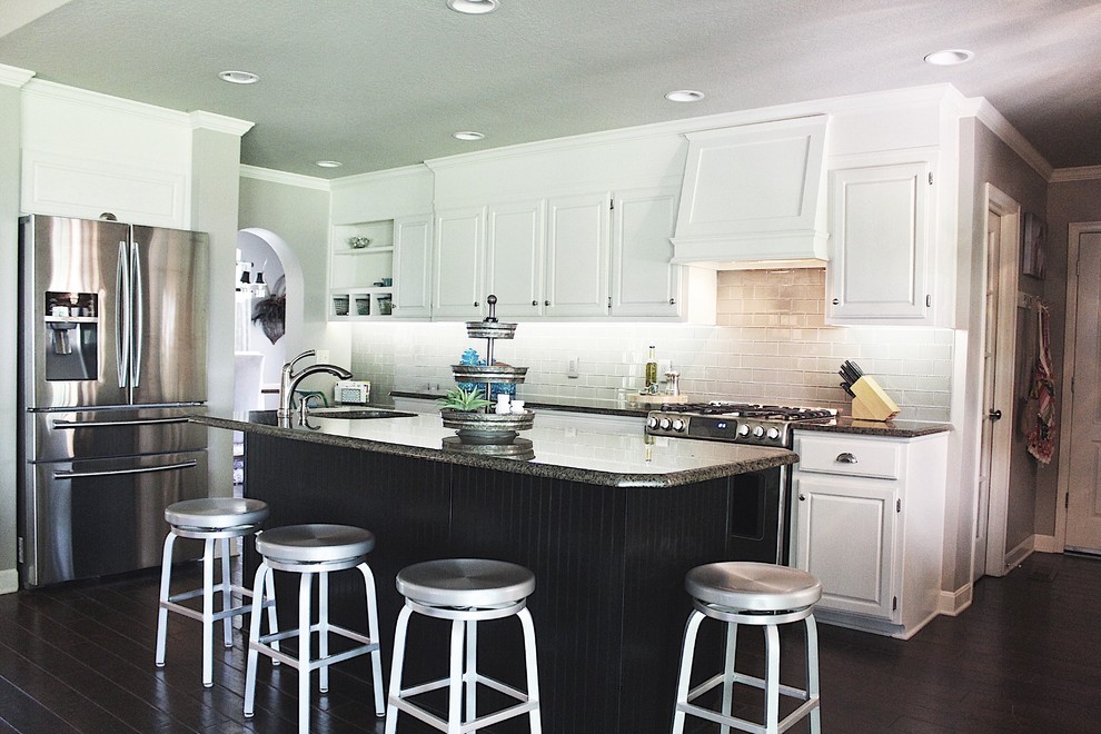 Mid-sized transitional l-shaped dark wood floor and brown floor enclosed kitchen photo with an undermount sink, raised-panel cabinets, white cabinets, granite countertops, gray backsplash, glass tile backsplash, stainless steel appliances and an island