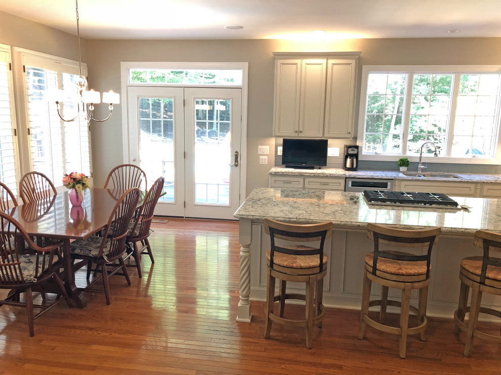 Photo of a large traditional l-shaped eat-in kitchen in Baltimore with a double-bowl sink, recessed-panel cabinets, white cabinets, quartz benchtops, grey splashback, subway tile splashback, stainless steel appliances, medium hardwood floors, with island, brown floor and grey benchtop.