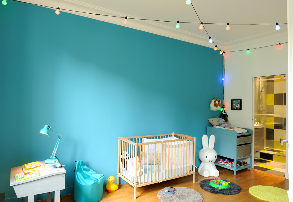 Photo of a contemporary gender-neutral kids' room in Paris with blue walls and light hardwood floors.