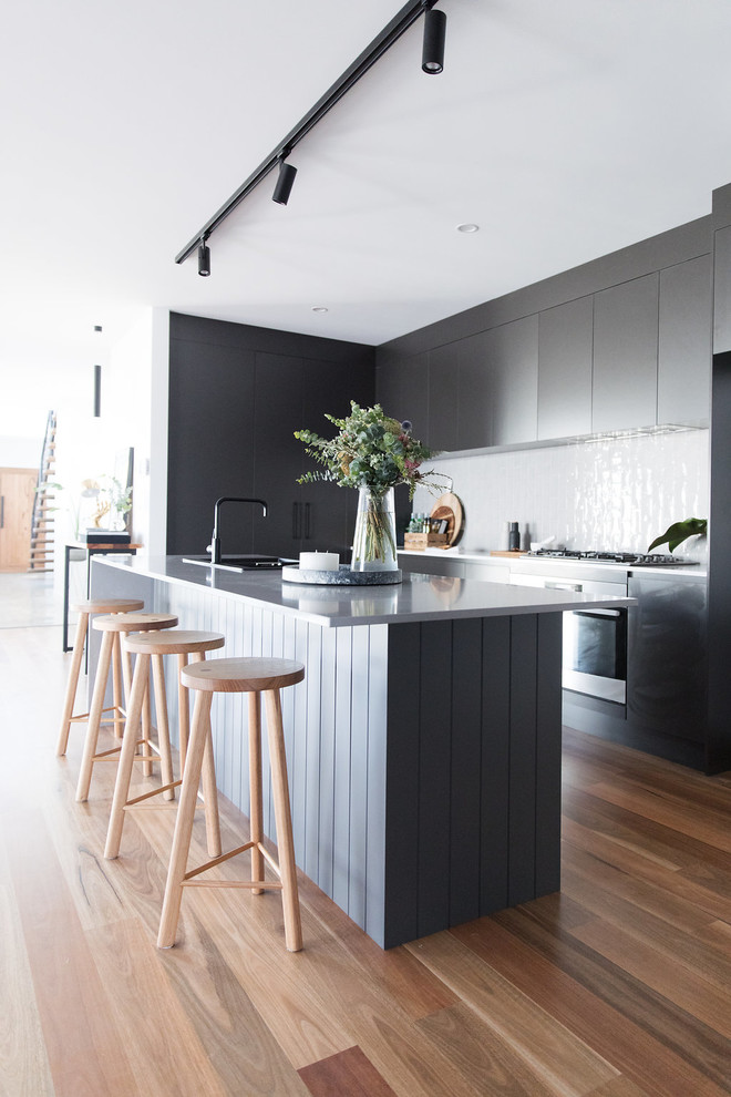 This is an example of a mid-sized contemporary l-shaped open plan kitchen in Canberra - Queanbeyan with a double-bowl sink, black cabinets, quartz benchtops, medium hardwood floors, with island, brown floor, flat-panel cabinets and white splashback.