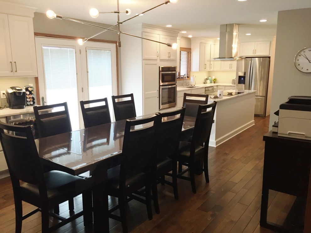 Example of a large transitional l-shaped dark wood floor eat-in kitchen design with an undermount sink, flat-panel cabinets, white cabinets, quartz countertops, white backsplash, ceramic backsplash, stainless steel appliances and an island