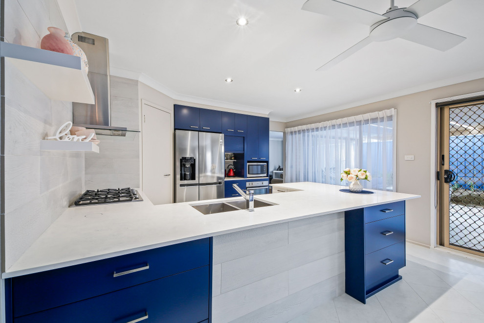 This is an example of a mid-sized beach style u-shaped eat-in kitchen in Central Coast with an undermount sink, flat-panel cabinets, blue cabinets, solid surface benchtops, subway tile splashback, stainless steel appliances, cement tiles, a peninsula, white floor and white benchtop.
