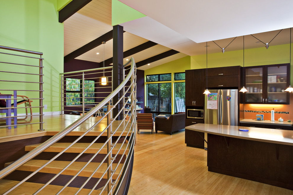 Modern open plan kitchen in San Francisco with flat-panel cabinets, dark wood cabinets, orange splashback and stainless steel appliances.