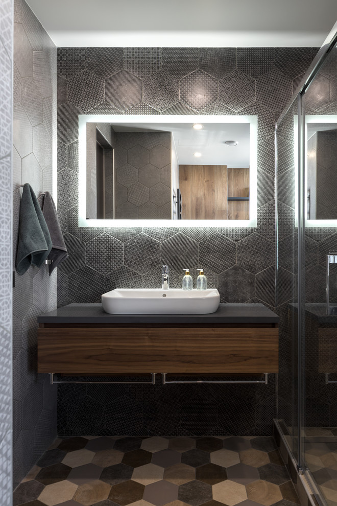 Photo of a large contemporary 3/4 bathroom in Moscow with flat-panel cabinets, dark wood cabinets, a corner shower, a wall-mount toilet, black tile, ceramic tile, grey walls, ceramic floors, a drop-in sink, solid surface benchtops, multi-coloured floor, a sliding shower screen and grey benchtops.
