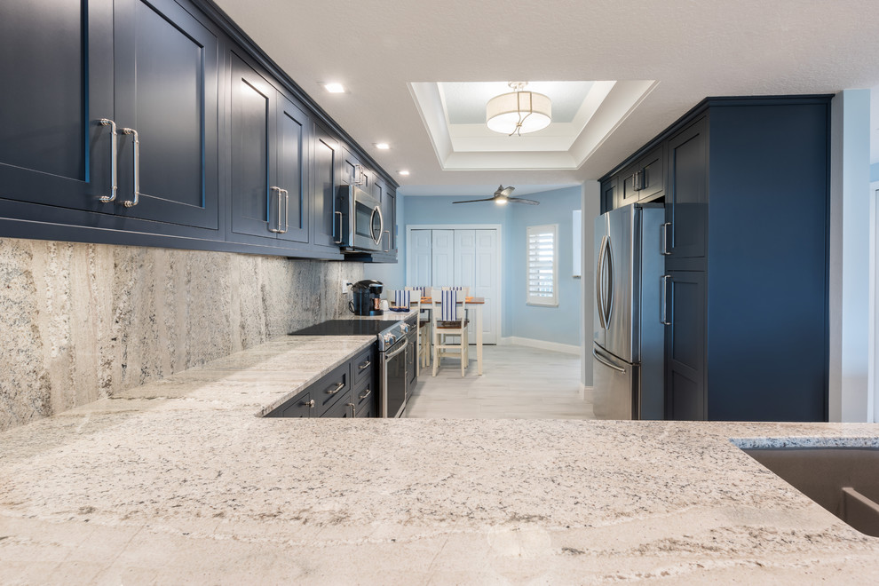 This is an example of a large transitional l-shaped eat-in kitchen in Orlando with an undermount sink, blue cabinets, granite benchtops, beige splashback, stone slab splashback, stainless steel appliances, porcelain floors, a peninsula, white floor and beige benchtop.