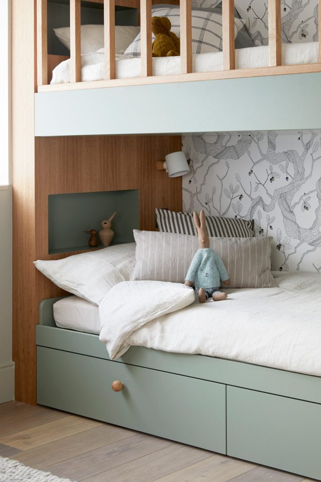 Photo of a large gender-neutral kids' bedroom for kids 4-10 years old in Wiltshire with white walls, medium hardwood floors and wallpaper.