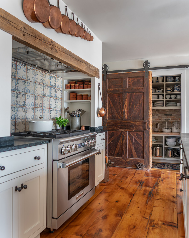 Inspiration for a country l-shaped kitchen in Boston with shaker cabinets, white cabinets, blue splashback, stainless steel appliances, light hardwood flooring, an island, black worktops, a single-bowl sink, porcelain splashback and exposed beams.