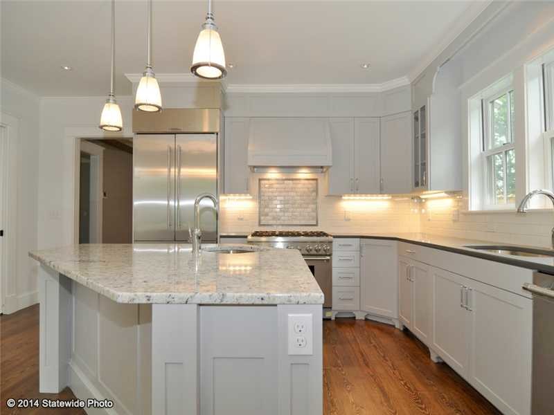Large transitional l-shaped medium tone wood floor kitchen photo in Providence with an undermount sink, shaker cabinets, white cabinets, granite countertops, white backsplash, subway tile backsplash, stainless steel appliances and an island
