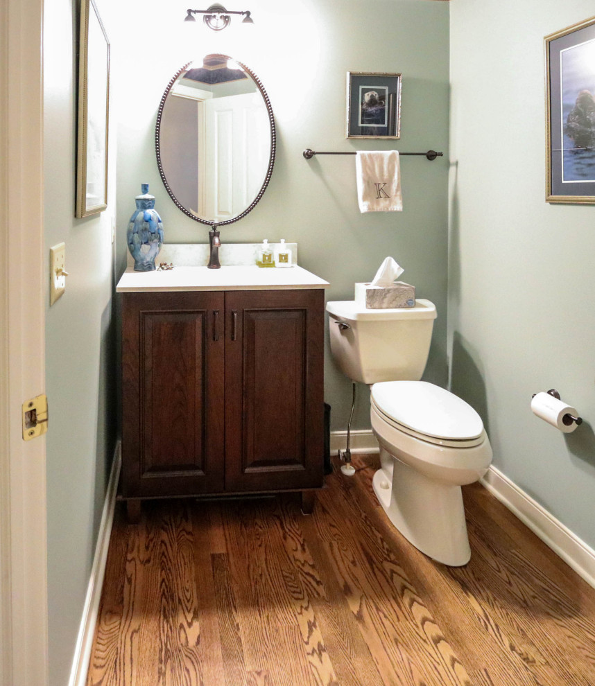 Cette image montre un petit WC et toilettes en bois foncé avec un placard avec porte à panneau surélevé, WC séparés, un mur vert, parquet foncé, un lavabo encastré, un plan de toilette en quartz modifié, un plan de toilette beige et meuble-lavabo sur pied.