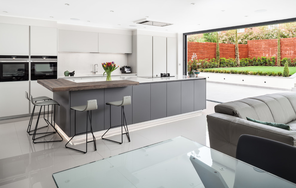 Large contemporary single-wall open plan kitchen in Surrey with flat-panel cabinets, white splashback, with island, white floor, white benchtop, black cabinets and black appliances.
