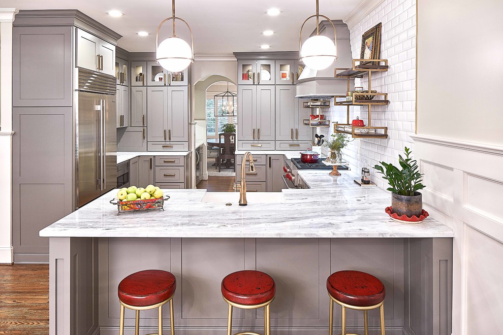 Inspiration for a mid-sized transitional u-shaped eat-in kitchen with a farmhouse sink, shaker cabinets, grey cabinets, marble benchtops, white splashback, subway tile splashback, stainless steel appliances, medium hardwood floors, a peninsula, brown floor and white benchtop.