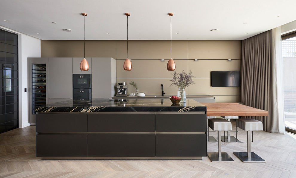 Photo of an expansive contemporary single-wall open plan kitchen in Dorset with an integrated sink, flat-panel cabinets, black cabinets, granite benchtops, metallic splashback, metal splashback, black appliances, with island, brown floor and black benchtop.