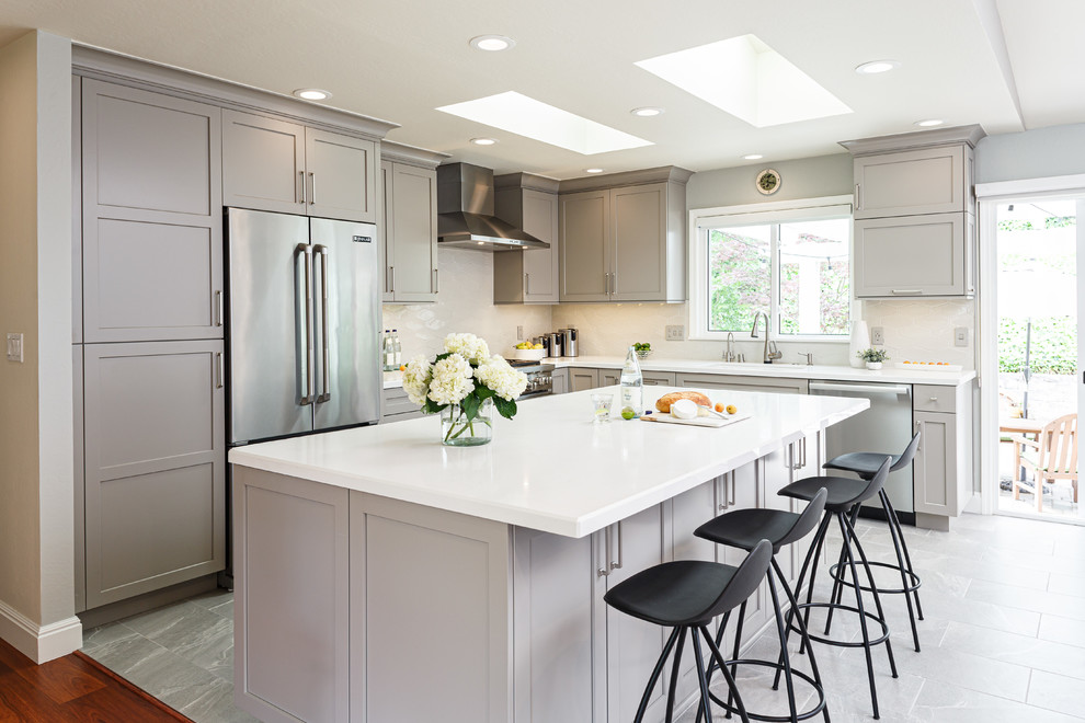 Inspiration for a transitional l-shaped kitchen in San Francisco with an undermount sink, shaker cabinets, grey cabinets, white splashback, stainless steel appliances, with island, grey floor and white benchtop.