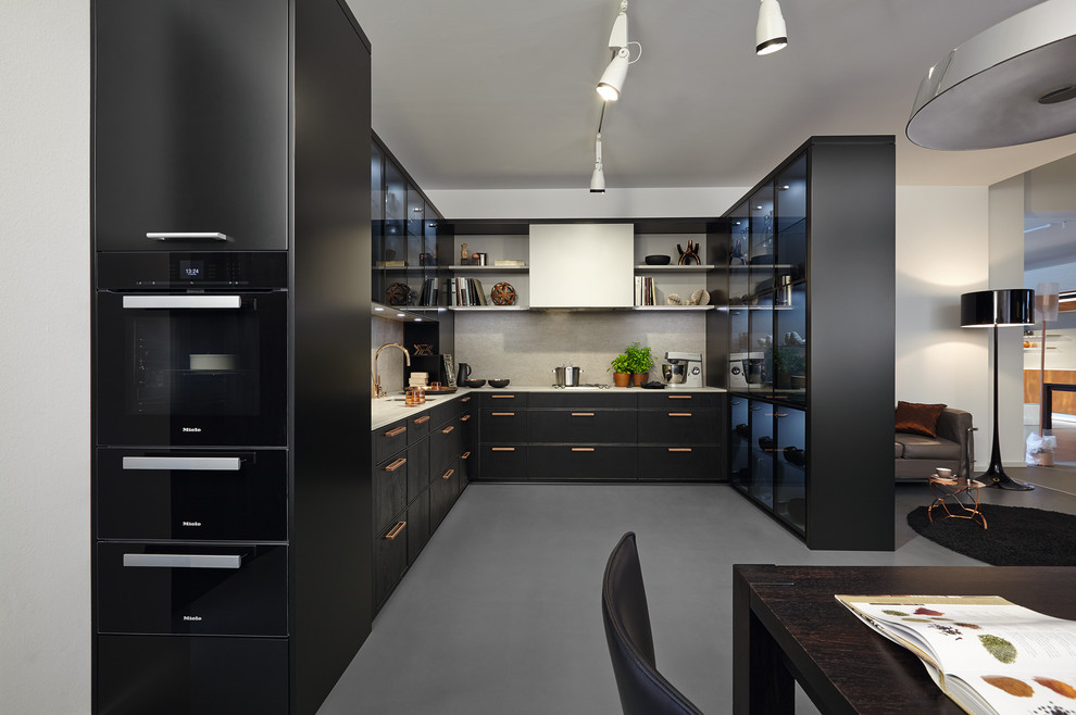 Inspiration for a large contemporary u-shaped open plan kitchen in Other with black cabinets, grey splashback, black appliances, concrete floors, no island and an undermount sink.