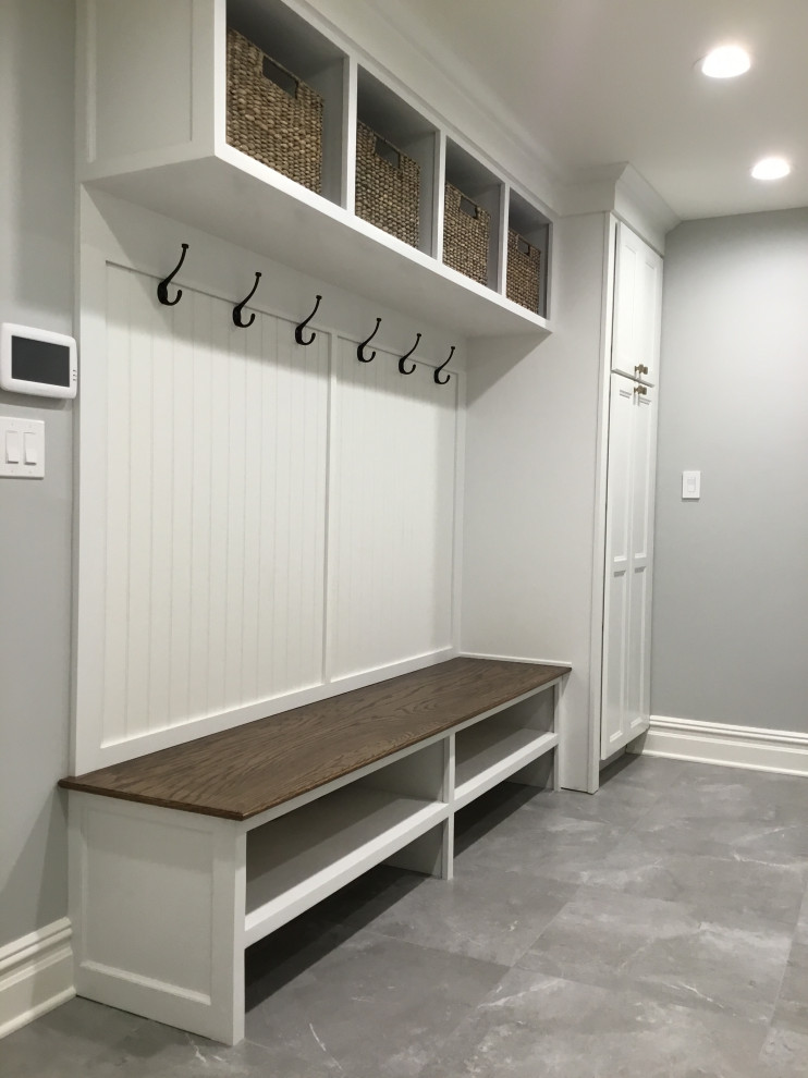 This is an example of a mid-sized country galley utility room in New York with an undermount sink, shaker cabinets, white cabinets, quartz benchtops, grey walls, ceramic floors, a stacked washer and dryer, grey floor and white benchtop.