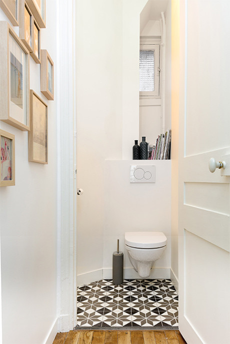 Small contemporary powder room in Paris with open cabinets, white cabinets, a wall-mount toilet, white tile, white walls, cement tiles, multi-coloured floor and white benchtops.