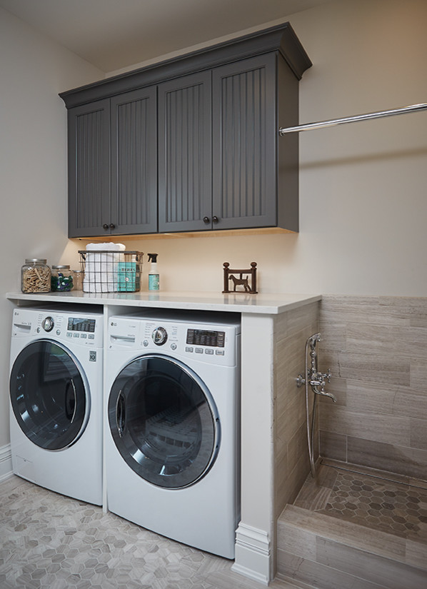 This is an example of a mid-sized traditional l-shaped dedicated laundry room in Grand Rapids with shaker cabinets, grey cabinets, quartz benchtops, beige walls, ceramic floors, a side-by-side washer and dryer and beige floor.