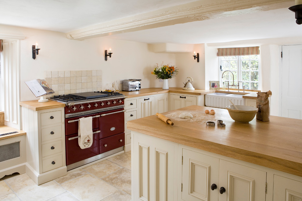 This is an example of a small country separate kitchen in Berkshire with a farmhouse sink, beige cabinets, wood benchtops, travertine floors and a peninsula.