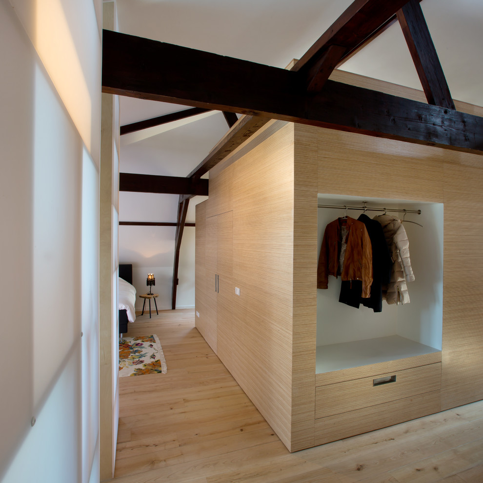 Photo of a modern gender-neutral built-in wardrobe in Amsterdam with flat-panel cabinets, light wood cabinets and light hardwood floors.