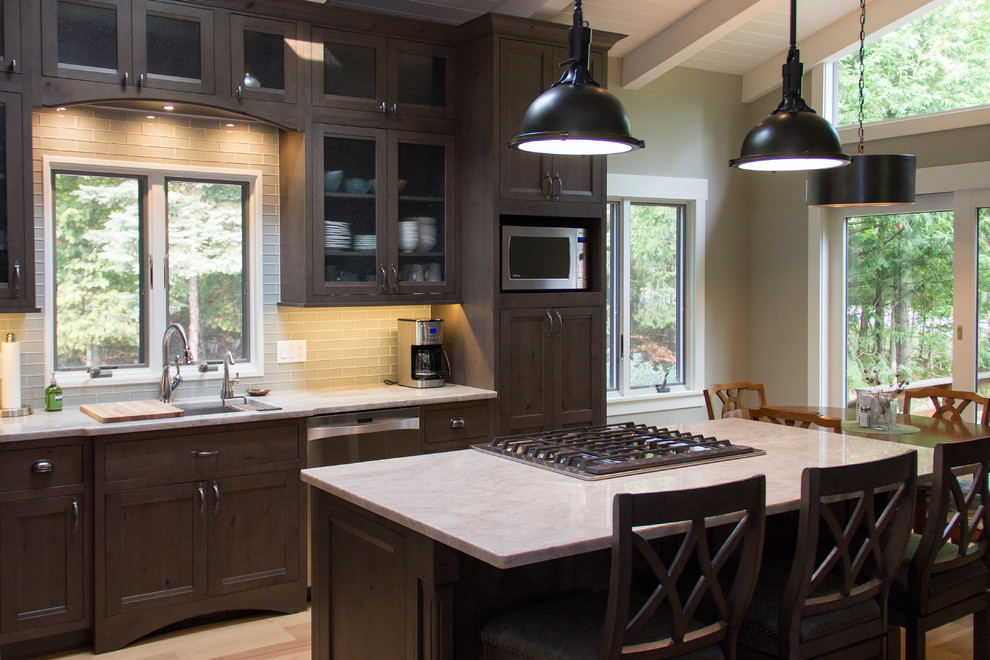 Eat-in kitchen - mid-sized transitional l-shaped light wood floor eat-in kitchen idea with an undermount sink, recessed-panel cabinets, dark wood cabinets, onyx countertops, gray backsplash, glass tile backsplash, stainless steel appliances and an island