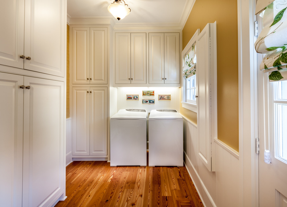 Photo of a traditional laundry room in Dallas with white cabinets, medium hardwood floors, a side-by-side washer and dryer and brown walls.