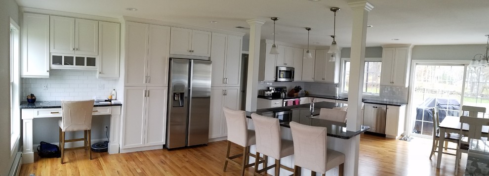 Large transitional l-shaped light wood floor and brown floor eat-in kitchen photo with an undermount sink, shaker cabinets, white cabinets, granite countertops, white backsplash, subway tile backsplash, stainless steel appliances and an island