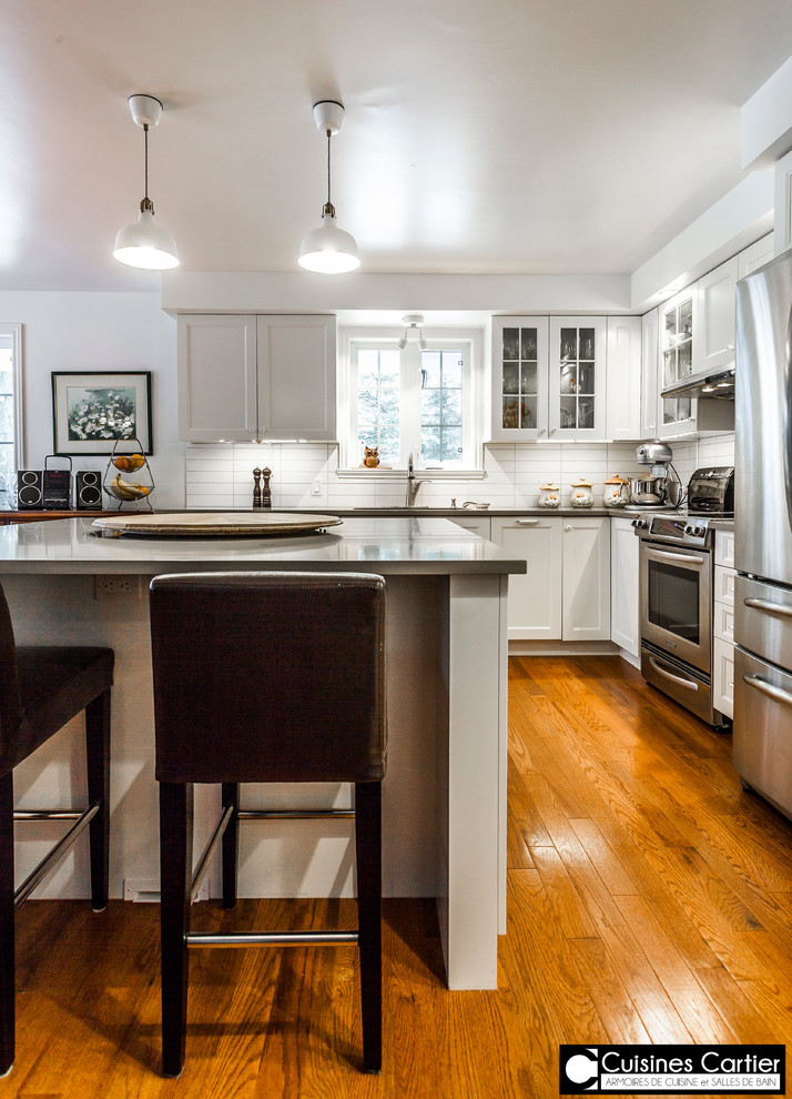 Inspiration for a large transitional medium tone wood floor eat-in kitchen remodel in Montreal with a double-bowl sink, shaker cabinets, white cabinets, quartzite countertops, white backsplash, ceramic backsplash, stainless steel appliances and an island