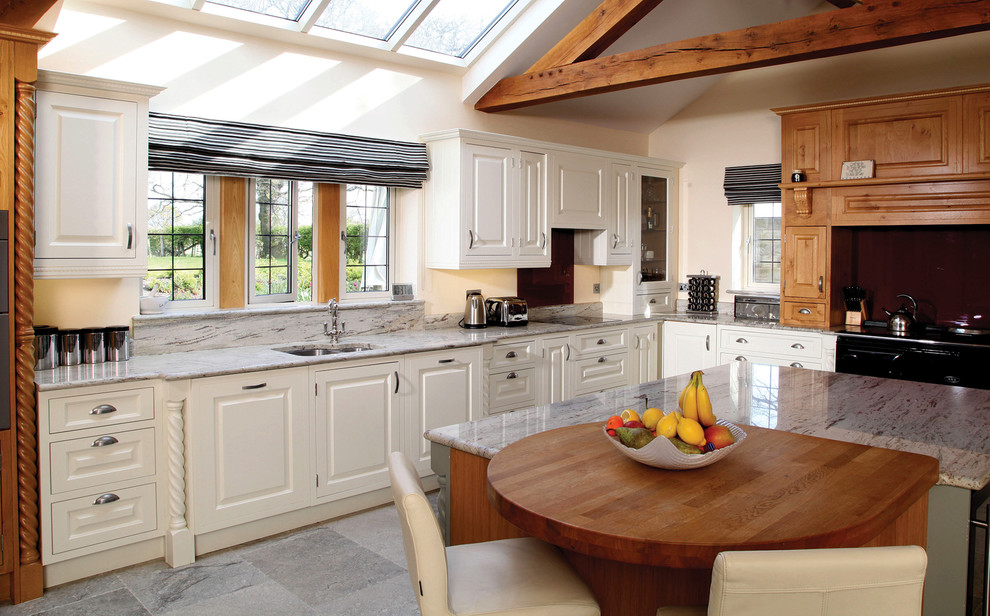 This is an example of a large traditional l-shaped kitchen with white cabinets, marble worktops, stainless steel appliances and an island.