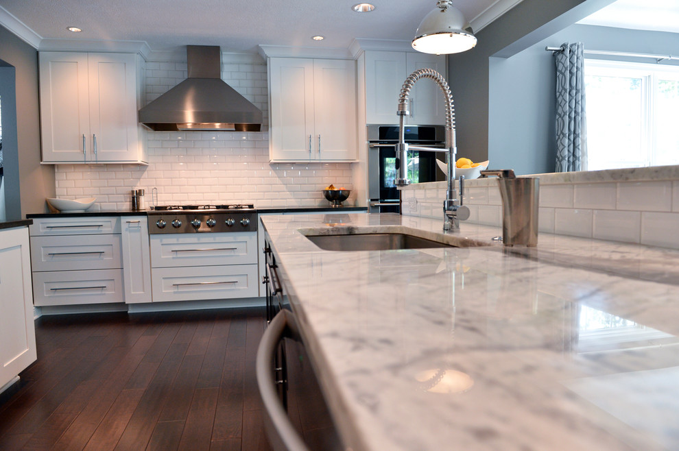 Inspiration for a transitional dark wood floor kitchen remodel in Cleveland with a drop-in sink, recessed-panel cabinets, white backsplash, ceramic backsplash, stainless steel appliances and an island