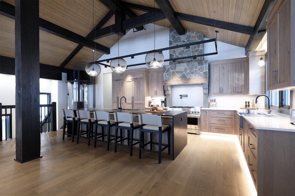Open concept kitchen - large rustic l-shaped medium tone wood floor, brown floor and exposed beam open concept kitchen idea in Vancouver with a farmhouse sink, shaker cabinets, medium tone wood cabinets, quartzite countertops, gray backsplash, porcelain backsplash, paneled appliances, an island and black countertops