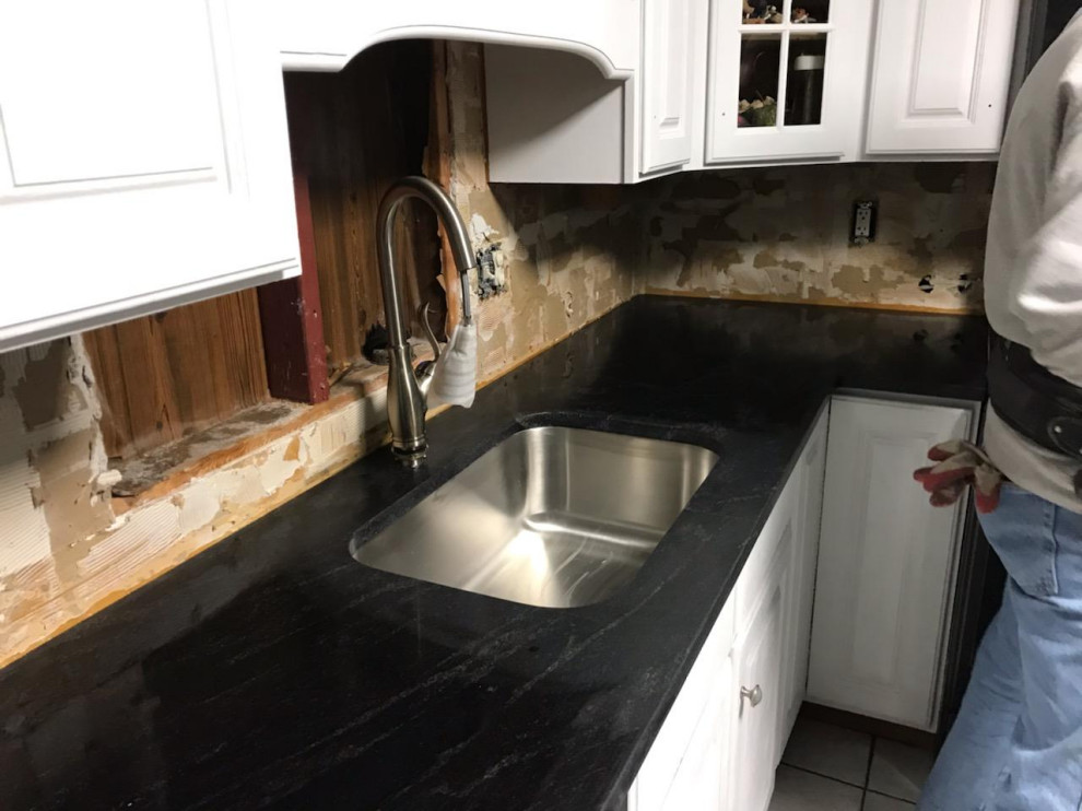 This is an example of a small l-shaped separate kitchen in Other with a single-bowl sink, raised-panel cabinets, white cabinets, granite benchtops, black splashback, stainless steel appliances, ceramic floors, no island, white floor and black benchtop.