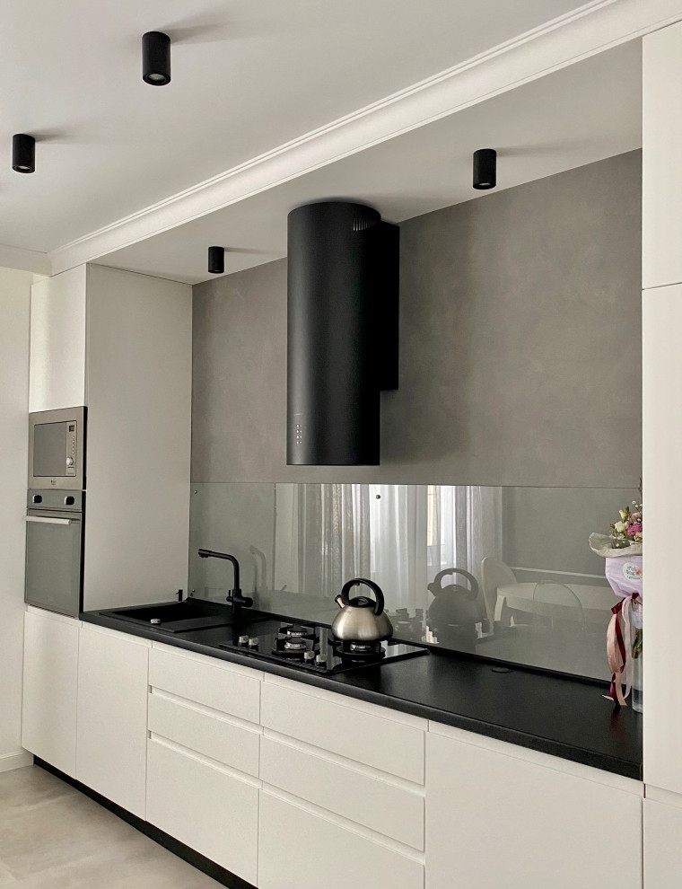 Contemporary single-wall eat-in kitchen in Other with an undermount sink, flat-panel cabinets, white cabinets, laminate benchtops, grey splashback, glass sheet splashback, black appliances, porcelain floors, no island, grey floor, black benchtop and recessed.