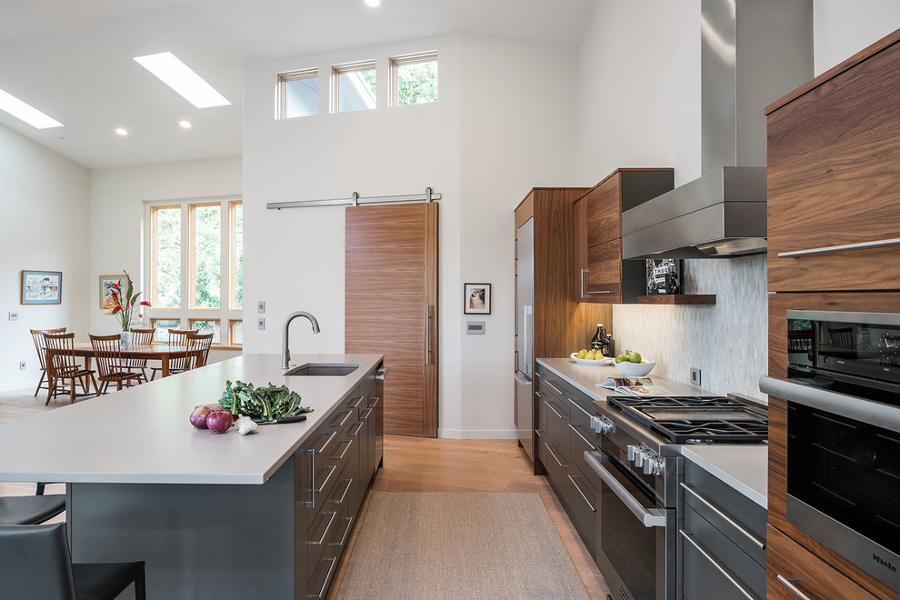 Inspiration for a contemporary galley open plan kitchen in Portland with an undermount sink, flat-panel cabinets, medium wood cabinets, quartz benchtops, grey splashback, ceramic splashback, stainless steel appliances, light hardwood floors and with island.