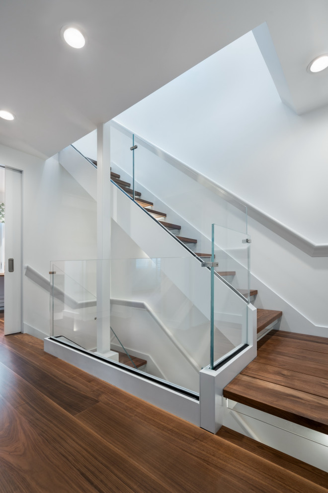 Cette image montre un petit escalier flottant minimaliste avec des marches en bois, des contremarches en verre et un garde-corps en verre.