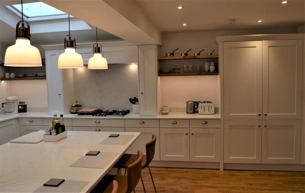 Photo of a mid-sized scandinavian l-shaped open plan kitchen in Sussex with shaker cabinets, white cabinets, quartzite benchtops, white splashback, engineered quartz splashback, black appliances, vinyl floors, with island, white benchtop and vaulted.
