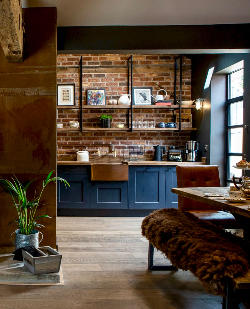 Inspiration for a medium sized bohemian l-shaped open plan kitchen with a belfast sink, shaker cabinets, black cabinets, wood worktops, brick splashback, medium hardwood flooring, no island, brown floors, brown worktops and a vaulted ceiling.