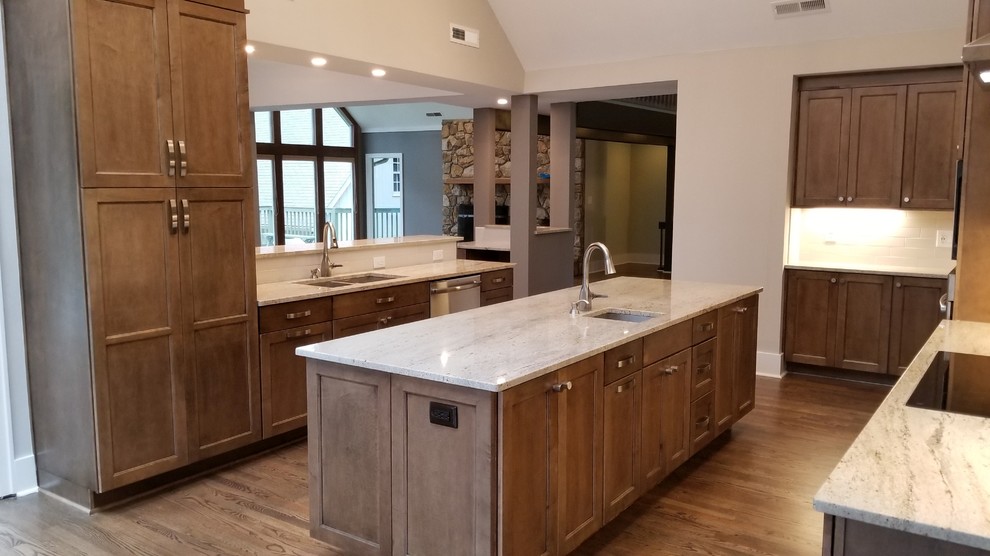 Photo of a large transitional u-shaped eat-in kitchen in Raleigh with an undermount sink, recessed-panel cabinets, dark wood cabinets, granite benchtops, white splashback, subway tile splashback, stainless steel appliances, medium hardwood floors, with island, brown floor and grey benchtop.