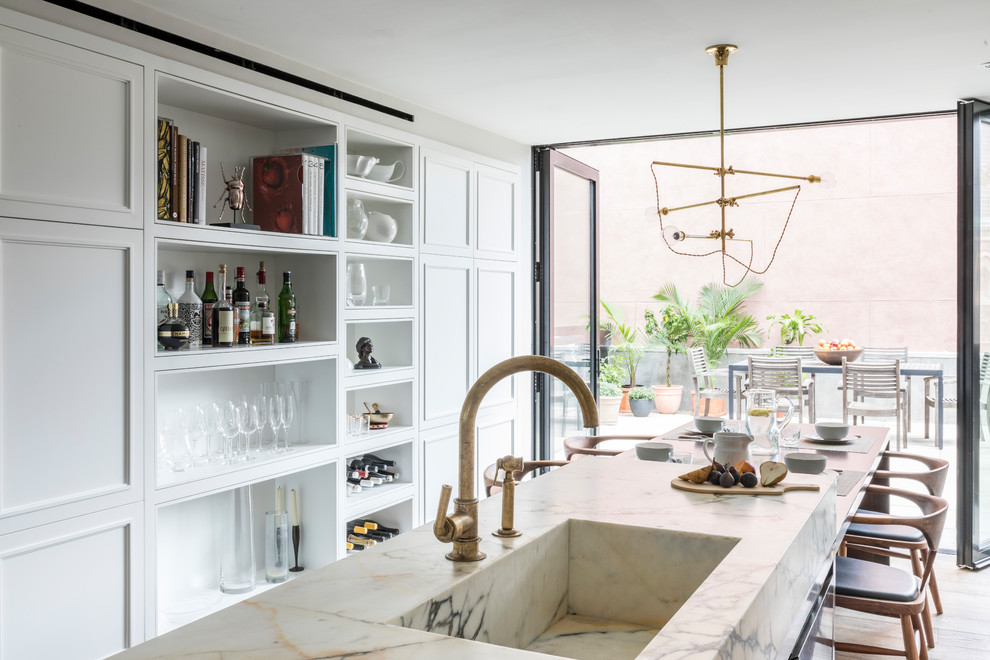 Photo of a mid-sized scandinavian single-wall open plan kitchen in New York with an integrated sink, shaker cabinets, white cabinets, marble benchtops, multi-coloured splashback, marble splashback, stainless steel appliances, dark hardwood floors, with island, brown floor and white benchtop.