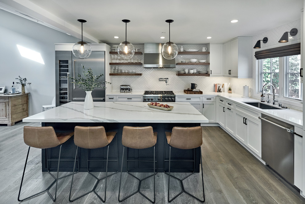 This is an example of a transitional kitchen in San Francisco with an undermount sink, shaker cabinets, white cabinets, white splashback, stainless steel appliances, light hardwood floors, with island, brown floor and white benchtop.