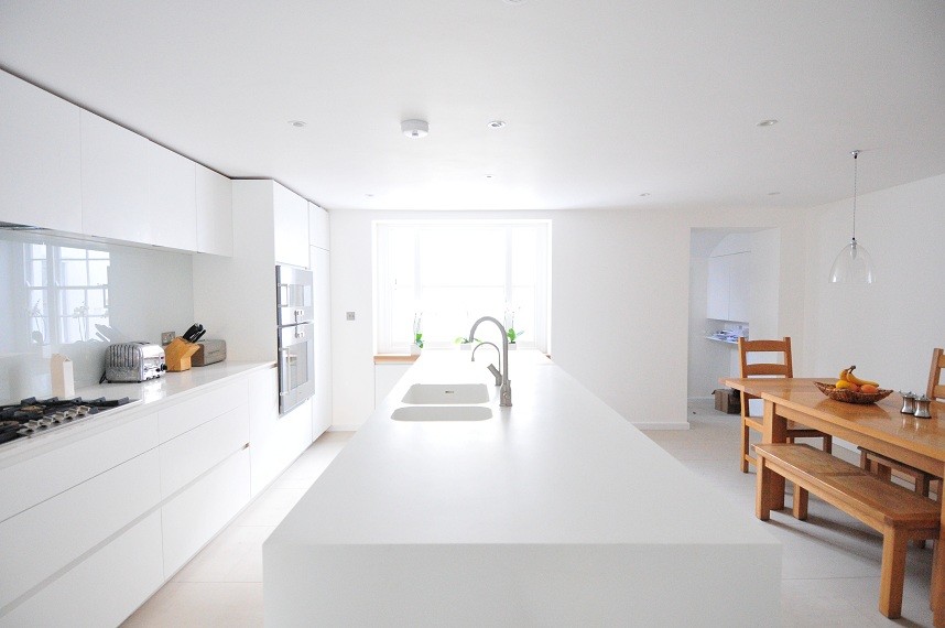 Inspiration for a large contemporary eat-in kitchen in London with flat-panel cabinets, white cabinets, glass sheet splashback, stainless steel appliances, with island, an undermount sink, solid surface benchtops, white splashback and porcelain floors.