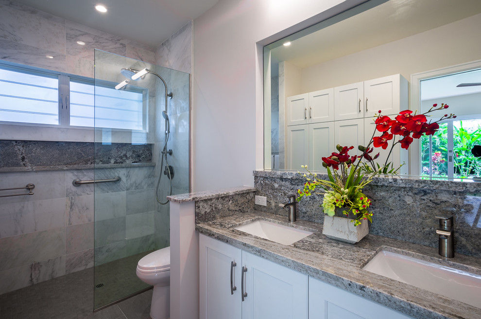 Inspiration for a large tropical master bathroom in Hawaii with shaker cabinets, white cabinets, gray tile, marble, granite benchtops, a curbless shower, a one-piece toilet, white walls, porcelain floors, an undermount sink, grey floor and an open shower.