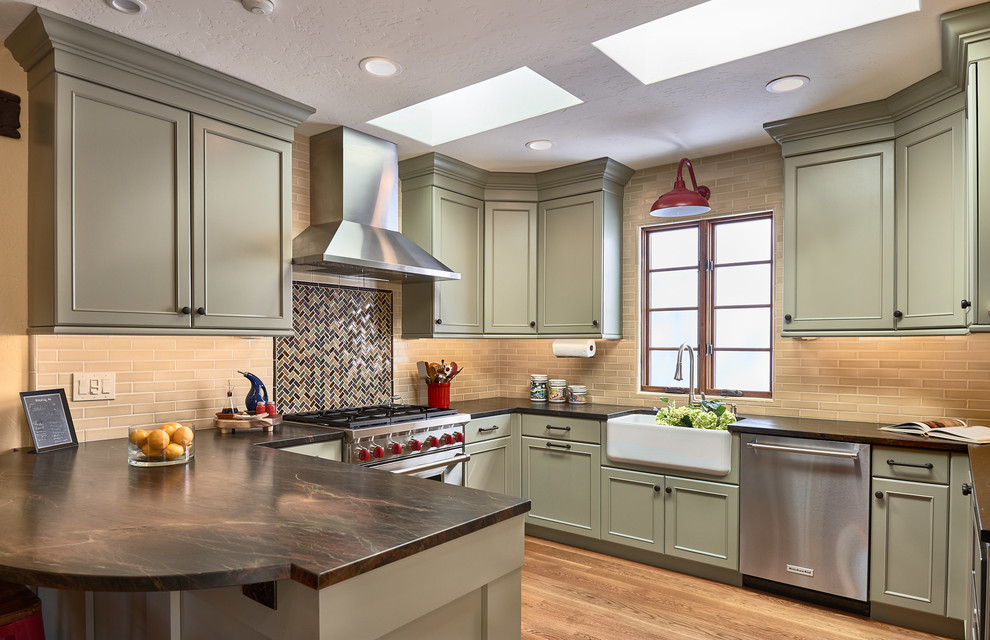 Photo of a traditional u-shaped kitchen in San Francisco with a farmhouse sink, recessed-panel cabinets, green cabinets, multi-coloured splashback, mosaic tile splashback, stainless steel appliances, light hardwood floors, a peninsula and brown benchtop.