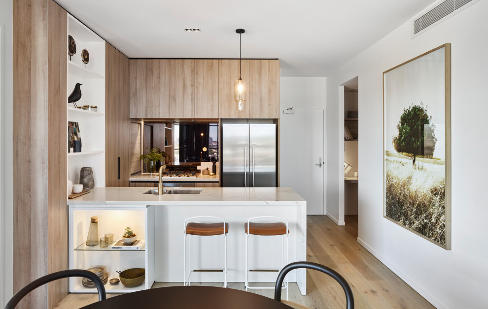 Design ideas for a contemporary u-shaped eat-in kitchen in Brisbane with an undermount sink, flat-panel cabinets, light wood cabinets, stainless steel appliances, light hardwood floors, a peninsula, beige floor and white benchtop.