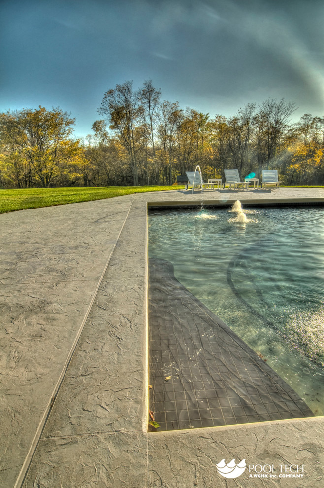 Aménagement d'une grande piscine arrière montagne rectangle avec un point d'eau et du béton estampé.